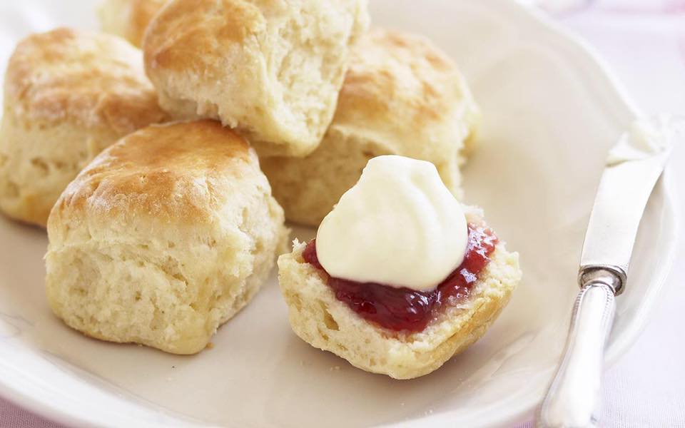 a plate of scones with one prepared with jam and cream on it.