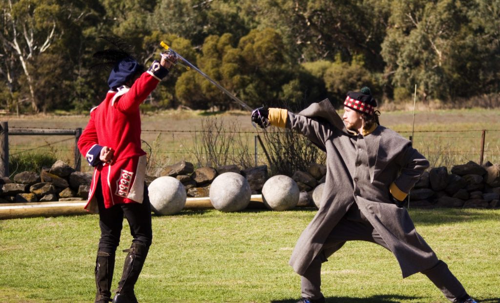 two sword fighters in Traditional soldier uniform sword fighting. one defending and one on right lunging forward .